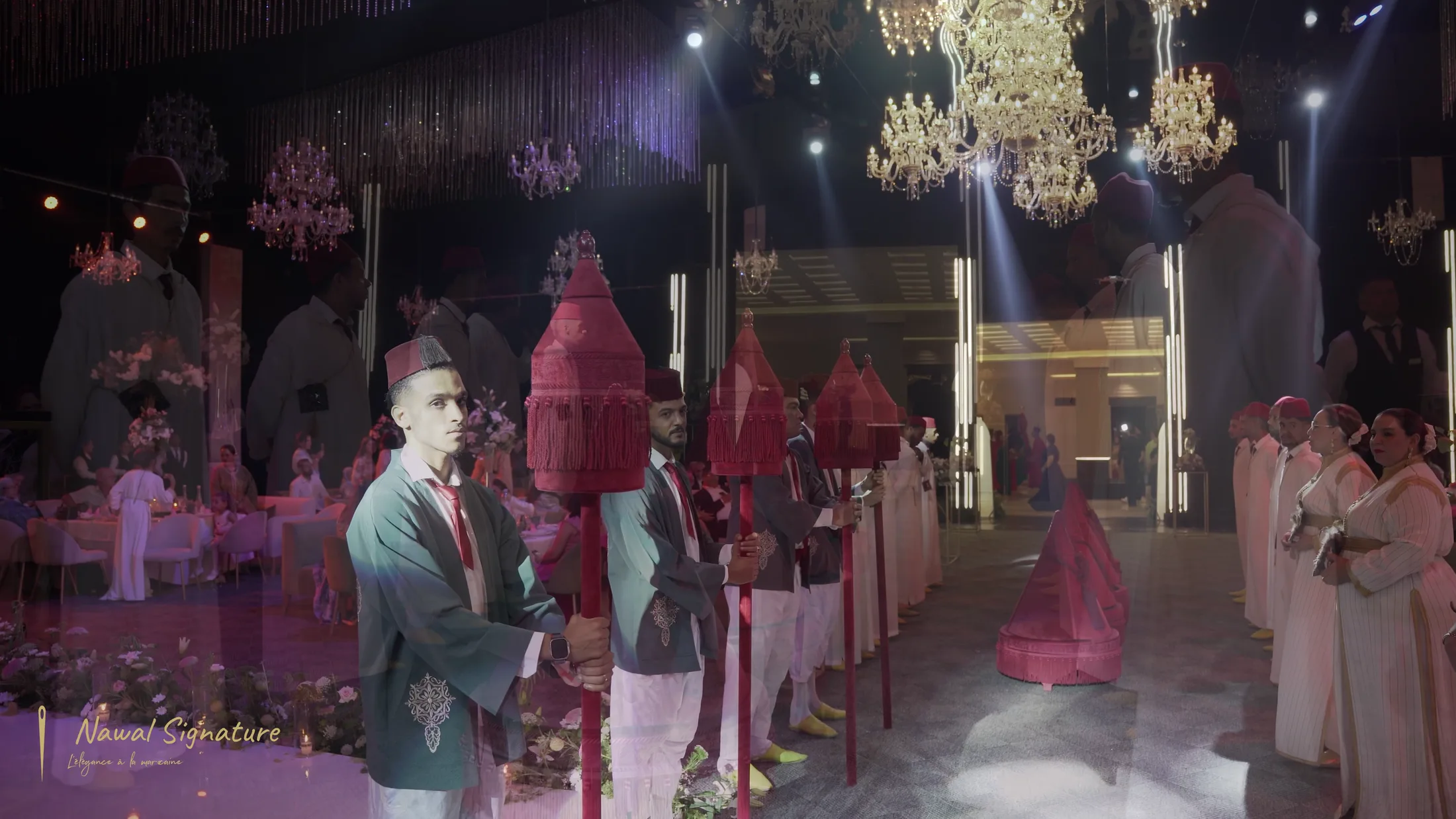 Cortège de porteurs sous les lustres d’une salle de réception, plateaux de velours rouge
